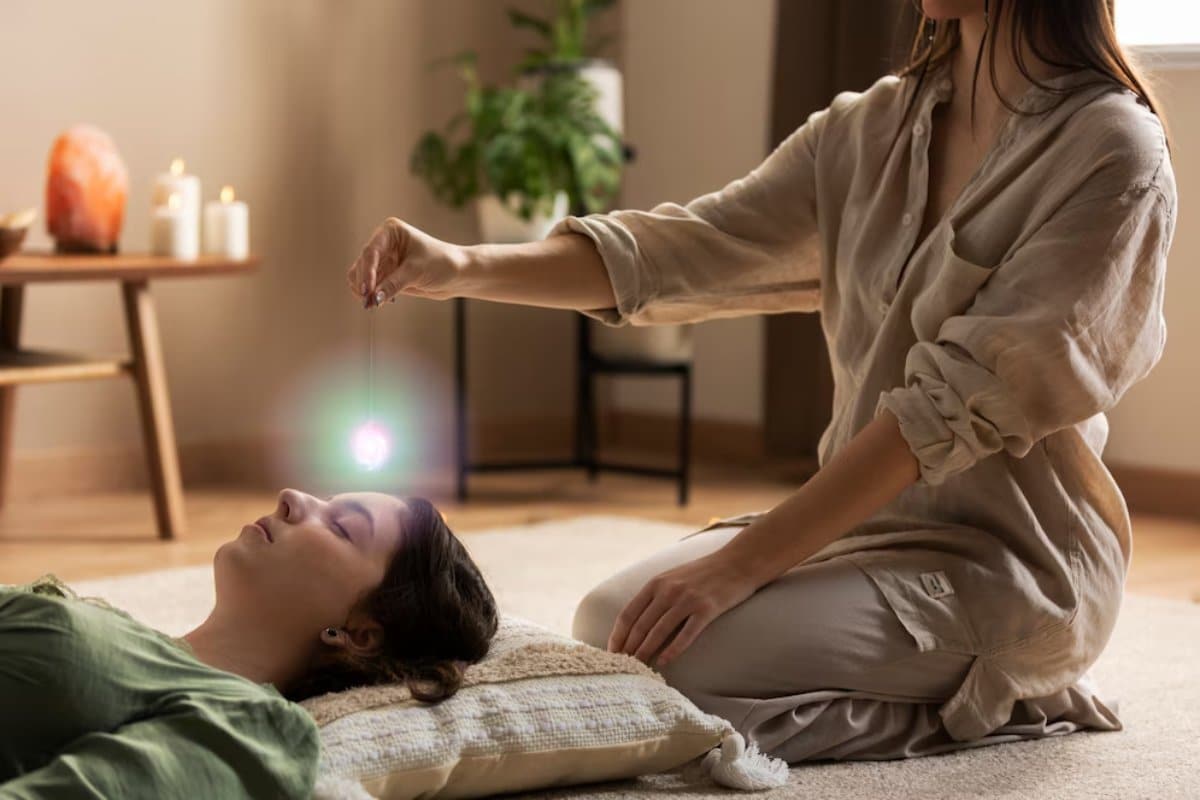 A woman performs a crystal healing session on another reclining woman in a serene indoor setting.