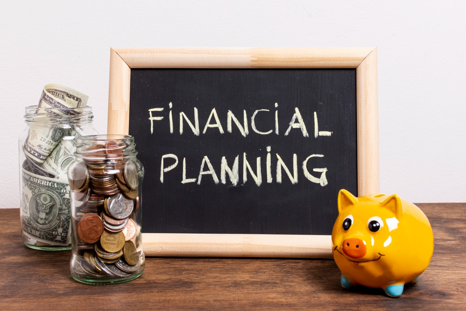 A chalkboard with Financial Planning written on it, flanked by jars of money and a piggy bank.