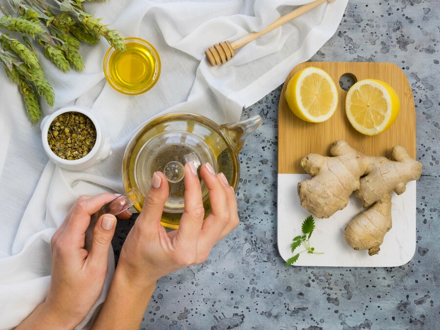 Hands preparing tea with ingredients like honey, lemon, and ginger on a textured tabletop.